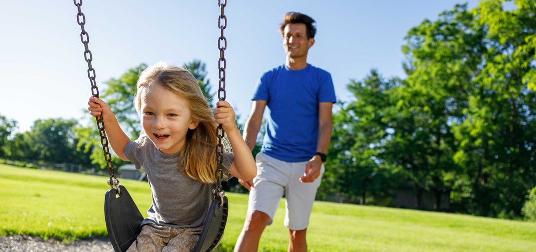 Man pushing daughter on swing while at the park