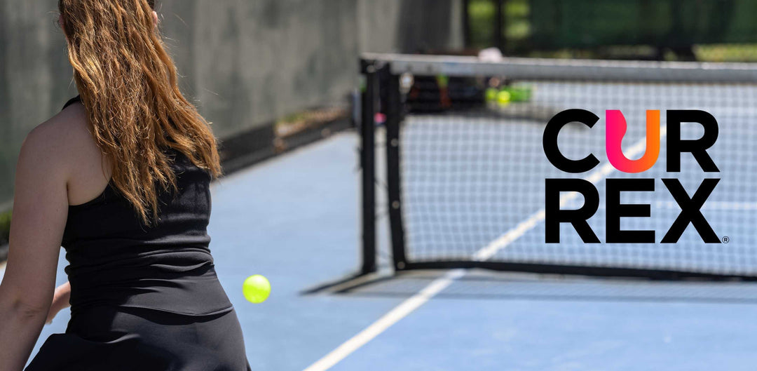 Shot from behind a woman about to hit a pickleball with the CURREX logo in the net