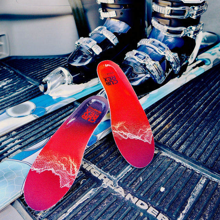 Pair of red low profile CURREX EDGEPRO insoles next to skis and ski boots #profile_high