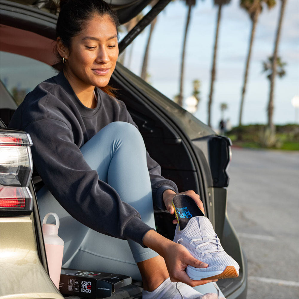 Woman placing CURREX RUNPRO high profile insole into gray running shoe #profile_high