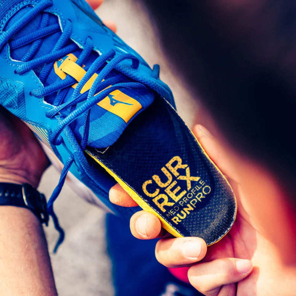 Man placing the CURREX RUNPRO medium profile insole into blue running shoe #profile_medium