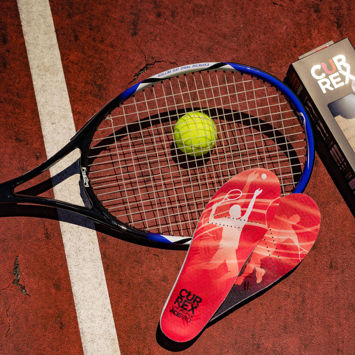 Pair of red low profile CURREX ACEPRO insoles sitting on tennis court next to tennis ball and racquet #profile_low