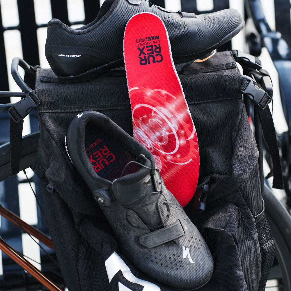 Black cycling shoes sitting against backpack with CURREX BIKEPRO red low profile insoles #profile_low