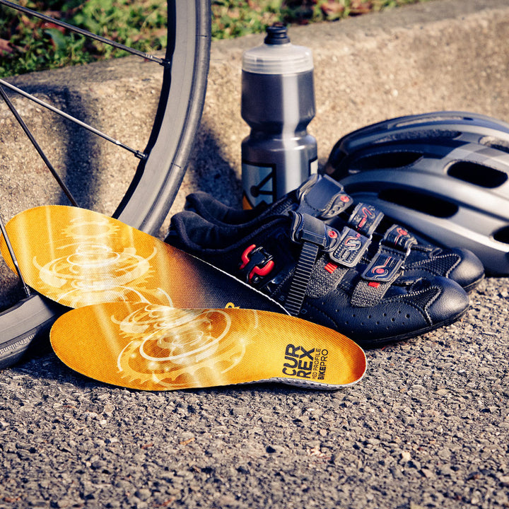 CURREX BIKEPRO yellow medium profile insoles sitting against bicycle wheel, cycling shoes, helmet, and water bottle. #profile_medium