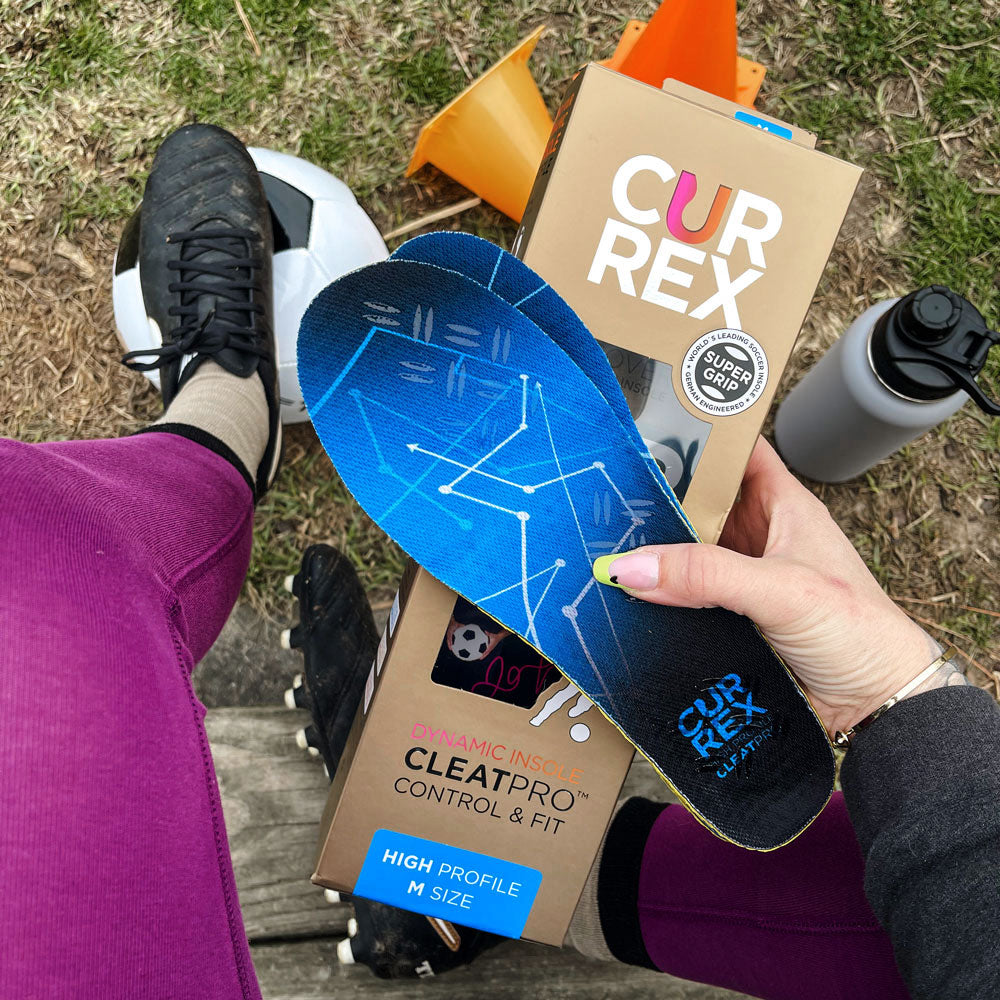 Woman sitting on bench with CURREX CLEATPRO blue high profile insoles in hand with water bottle and soccer ball below