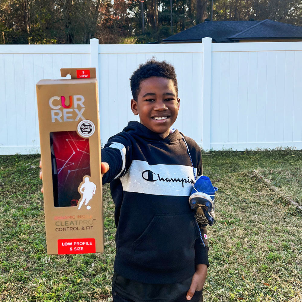 Little boy standing outside holding up a pair of CURREX CLEATPRO red low profile insoles