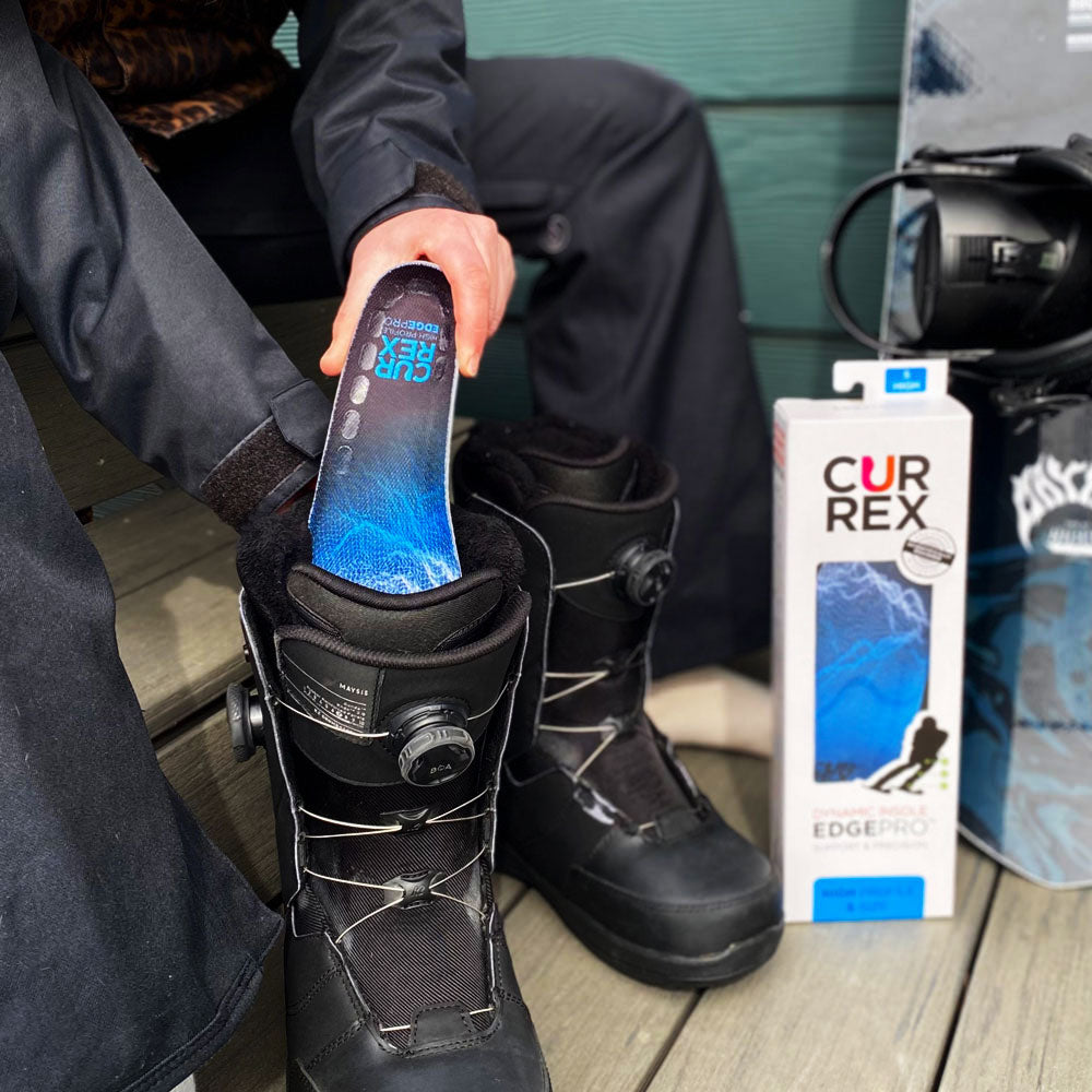 Person sitting on bench preparing to go skiing by placing CURREX EDGEPRO blue high profile insoles into black ski boots #profile_high