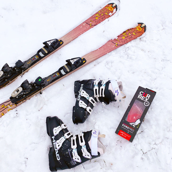 Skis, black ski boots, and CURREX EDGEPRO low profile red insoles sitting in the snow #profile_low