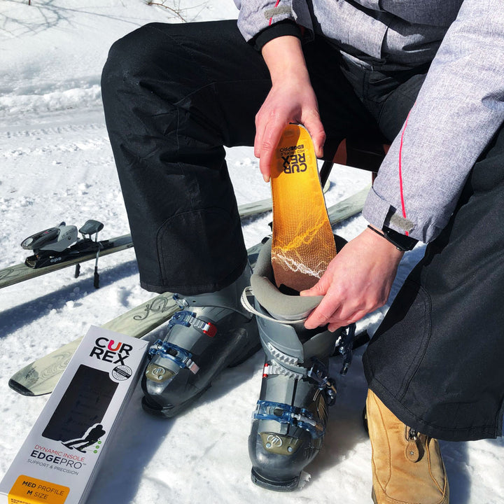 Man sitting on chair next to skis preparing to go skiing by adding CURREX EDGEPRO yellow medium profile insoles to ski boots #profile_medium