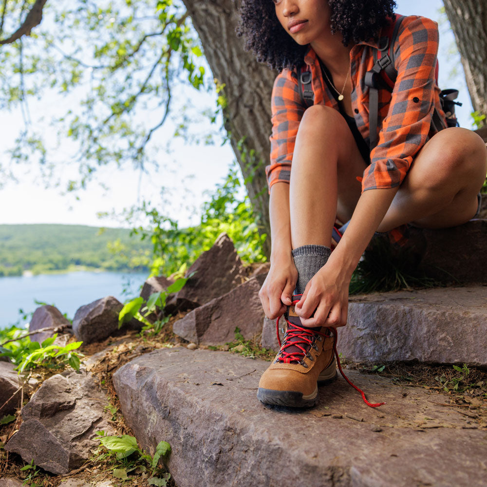 Woman taking a break from hiking to tie hiking shoe #profile_high