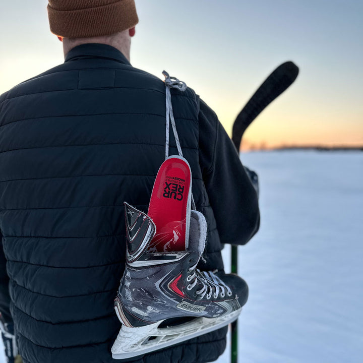 Man walking in the snow with hockey stick and black hockey skates with CURREX HOCKEYPRO red low profile insoles inside #profile_low