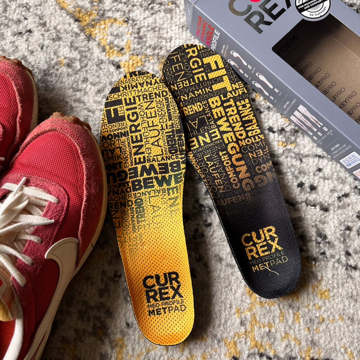 CURREX METPAD yellow medium profile insoles sitting on carpet next to red sneakers #profile_medium