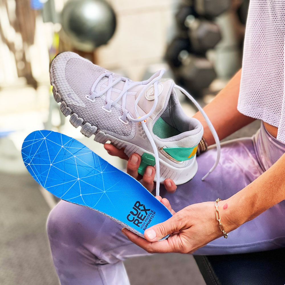 Woman preparing for her workout, holding up a cream colored sneaker and CURREX SUPPORTSTP blue high profile insole #profile_high