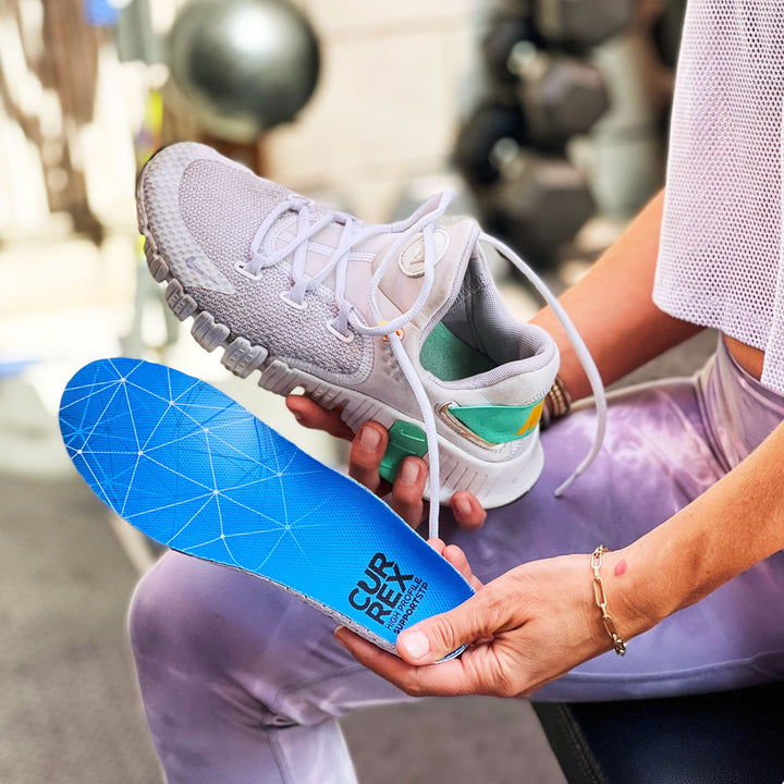 Woman preparing for her workout, holding up a cream colored sneaker and CURREX SUPPORTSTP blue high profile insole #profile_high