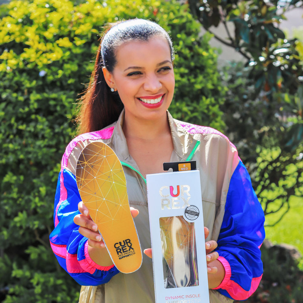 Woman standing outside holding up a pair of yellow medium profile CURREX SUPPORTSTP insoles #profile_medium